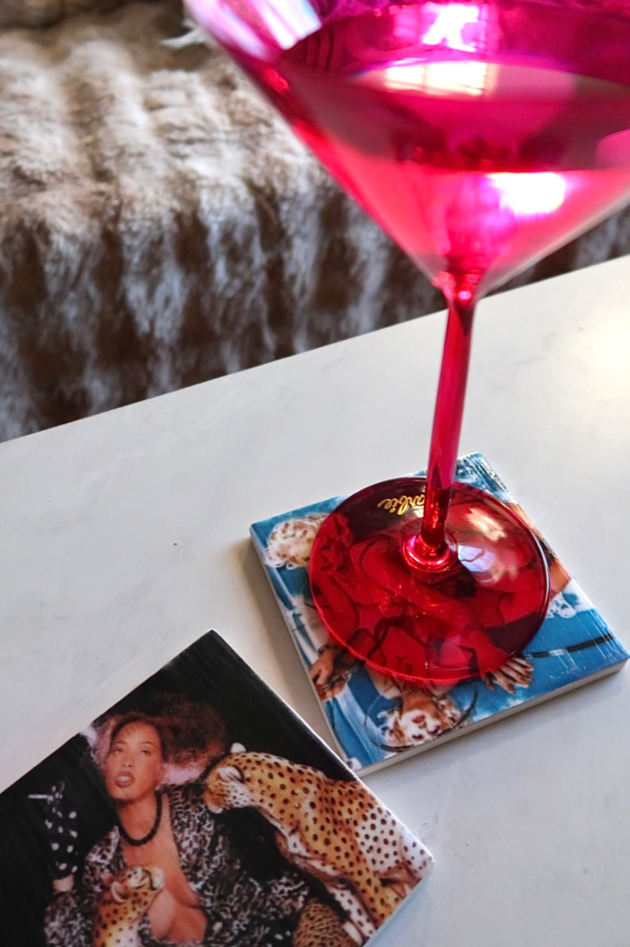 Pink martini glass resting on an Icon Coaster with a retro movie still